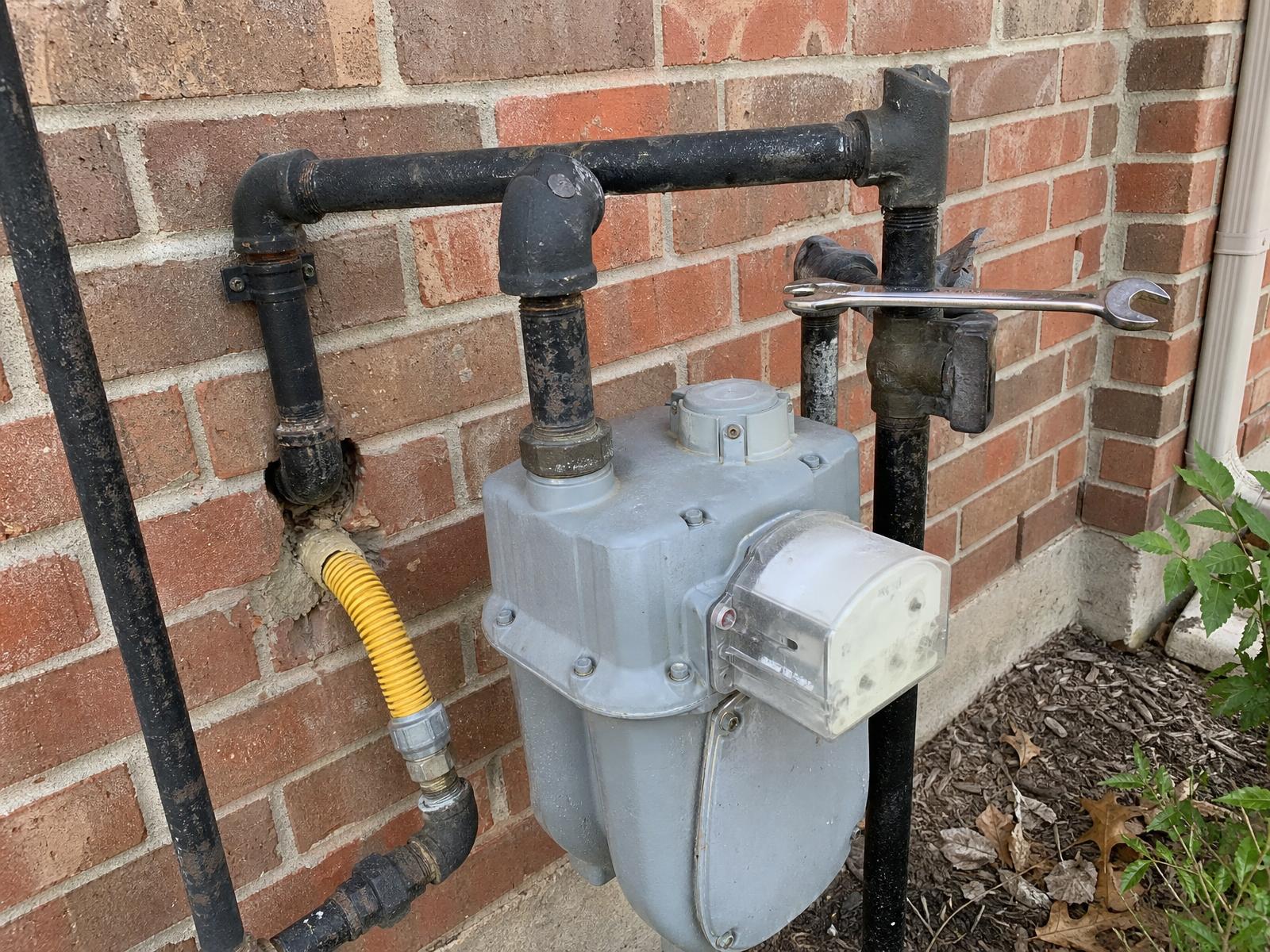 Exterior residential gas meter with black iron piping, yellow flex line and a wrench resting on the shutoff valve
